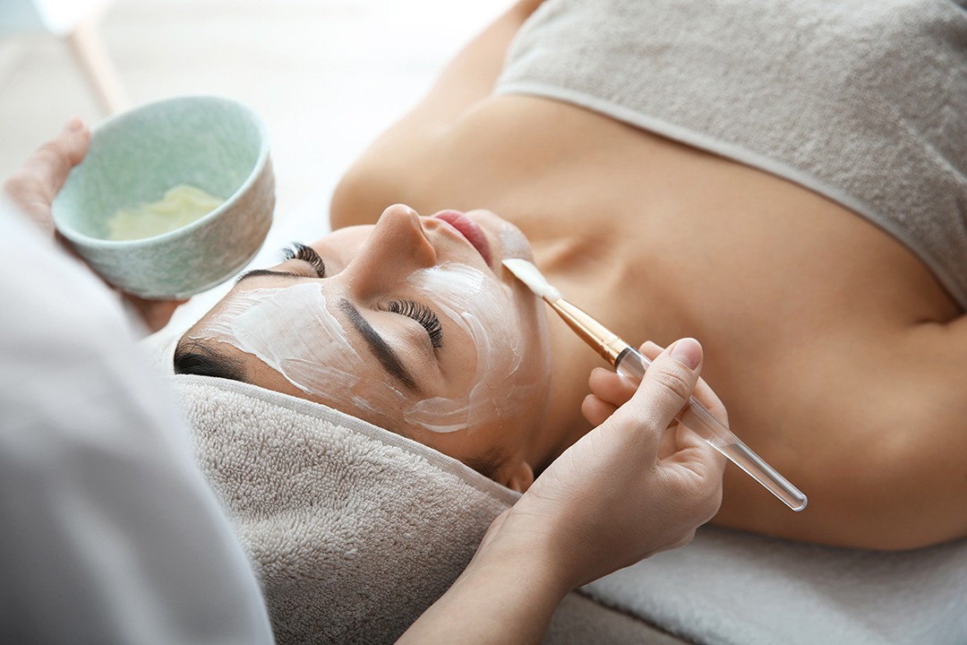 Cosmetologist applying mask on client’s face in spa salon